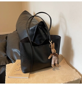 Detail of black leather tote bag with plush rabbit charm on stone pedestal