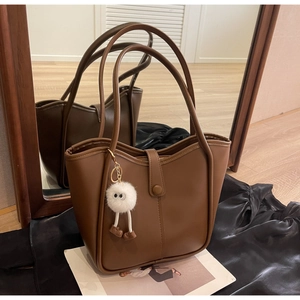 Dettaglio borsa tote in pelle marrone con ciondolo a mostro in peluche bianco su seta