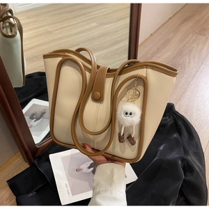 Dettaglio della borsa tote crema con bordi marroni e ciondolo in peluche in foto lifestyle