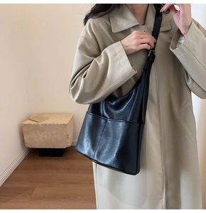 Dettaglio borsa a secchiello in pelle nera con tracolla larga su un trench elegante