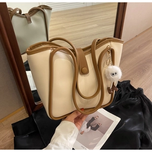 Dettaglio di una borsa tote color crema con bordo marrone e ciondolo a forma di mostro