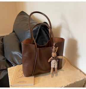 Detail of dark brown leather tote bag texture with cute plush bunny charm on stone pedestal