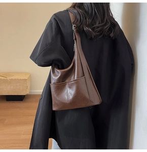 Dettaglio borsa a secchiello hobo in pelle marrone scuro con due tasche frontali sulla modella