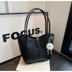 Dettaglio della borsa tote nera minimalista con trama opaca e ciondolo a pompon bianco