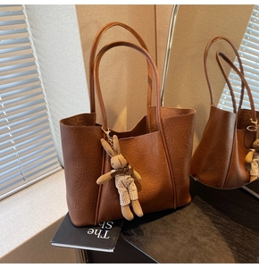 Detail of a brown leather tote bag featuring a knitted rabbit charm and pleated texture