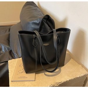 Close-up of black leather tote bag with white contrast stitching on stone surface