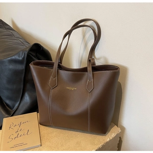 Detail of brown leather tote bag with white contrast stitching and gold lettering logo
