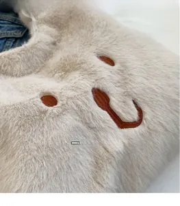 Nahaufnahme der flauschigen cremefarbenen Plüschtasche mit besticktem Bärengesicht