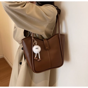 Close-up of brown matte leather tote bag with a buckle and white furry doll charm detail
