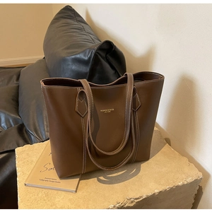 Macro detail of dark brown leather tote with white stitching and gold branding