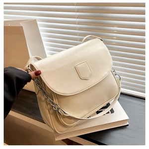 Detail view of cream-colored leather crossbody bag with silver chain and minimalist shield
