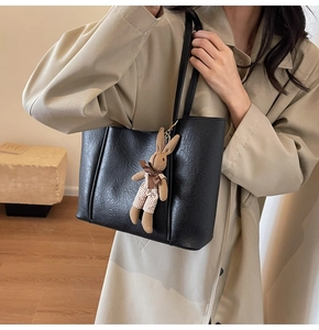 Detail of black textured tote bag with a brown plush rabbit charm on a beige background