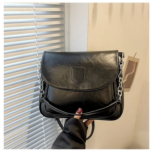 Close-up of black glossy PU leather shoulder bag with silver chain and artistic lighting