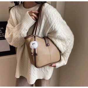 Dettaglio della borsa tote beige con finiture marroni e ciondolo a mostro di peluche sulla tracolla