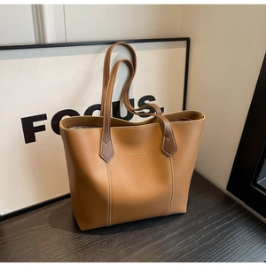 Close-up of brown leather tote bag with white stitching and gold foil lettering detail