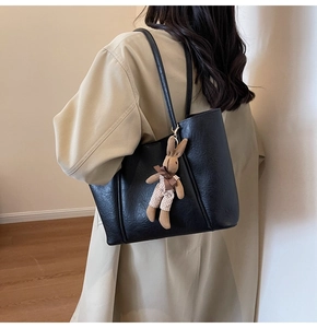 Close-up of black leather tote bag with brown plush bunny pendant and slim shoulder straps