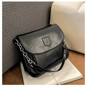 Detail of a vintage black faux leather crossbody bag with shield flap and chain strap