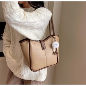 Detail of a large beige tote bag with brown trim and a plush white monster charm