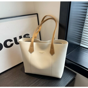 Close-up of minimalist leather tote bag with brown straps and gold logo on wooden surface