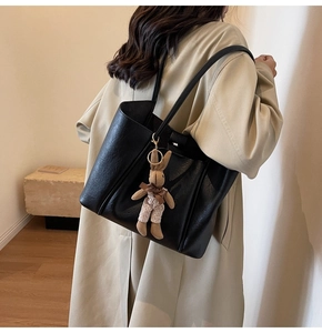 Detail of black pebbled tote bag with a brown plush rabbit charm on a beige trench coat