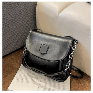 Detail of black glossy leather shoulder bag with silver chain on fashion magazine