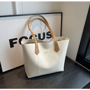 Detail view of large cream tote bag with brown handles and golden fashion text