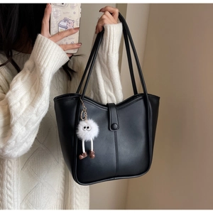 Detail of black faux leather tote bag with white plush monster charm on shoulder strap