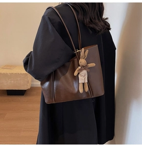 Detail of dark brown faux leather tote bag featuring a cute knitted rabbit charm and dual straps