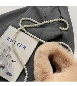 Detail of soft plush handbag with elegant white pearl bead strap on textured fabric