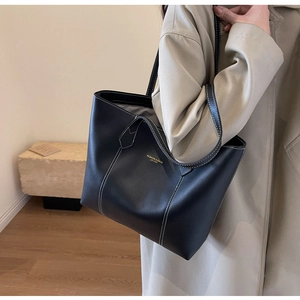 Detail of black tote bag with white contrast stitching and gold logo on front