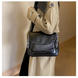 Detail of black vintage faux leather handbag featuring bold silver chain and flap closure