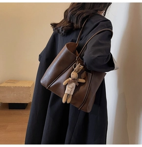 Brown leather tote bag worn over the shoulder featuring a cute bunny charm accessory