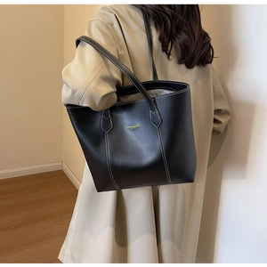 Detail of a large black leather tote bag with white contrast stitching and gold lettering
