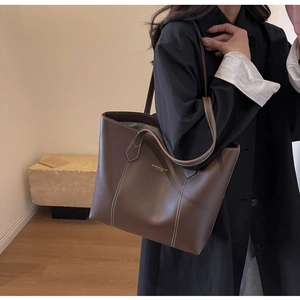 Detail of a large brown leather tote bag with white stitching and brand gold lettering