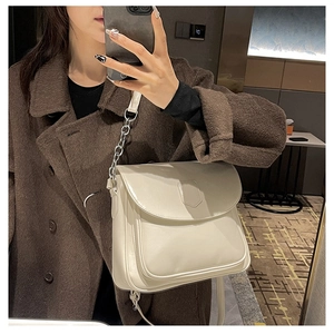 Close-up of cream faux leather crossbody bag with silver chain strap on tweed coat