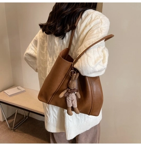 Brown leather tote bag featuring a cute rabbit charm shown on a woman shoulder