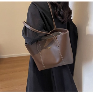 Close-up of brown leather tote bag showing white contrast stitching and gold lettering