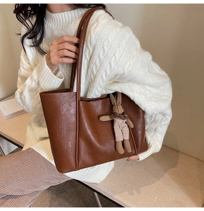 Detailed view of the brown leather tote bag with a cute plaid rabbit plush pendant charm