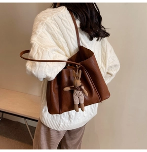 Detail of brown faux leather tote bag with plush rabbit charm on autumn sweater outfit