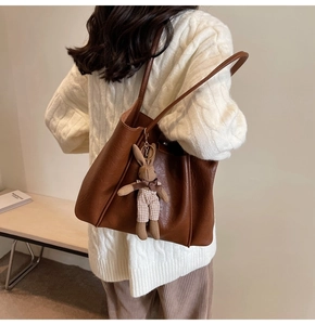 Detail of dark brown tote bag featuring a cute rabbit plush pendant and textured leather