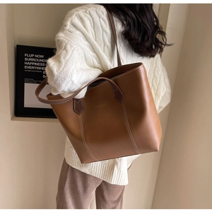 Detailed view of dark brown leather tote bag with contrast white stitching and long straps