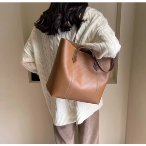 Brown leather tote bag with white contrast stitching and gold logo shown on model