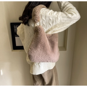 Close-up of plush faux fur shoulder bag with gold metal rings and thick knit sweater