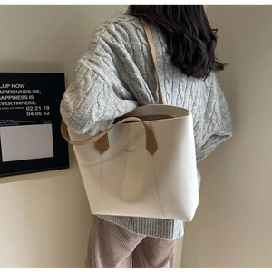 Detail of cream leather tote bag with brown handles worn with a grey knit sweater
