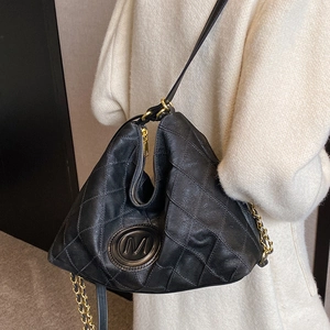 Sac fourre-tout noir matelassé avec logo M doré porté par un mannequin en pull