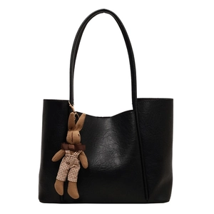 Minimalist black faux leather tote bag with a brown knitted bunny charm on white background