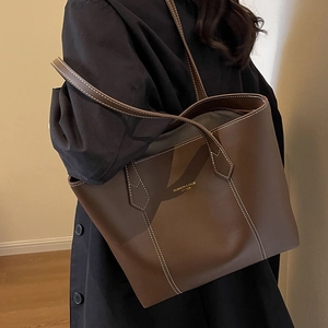 Brown tote bag with white contrast stitching and gold lettering in a daily commute scene