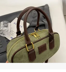 Dettaglio della borsa Boston in camoscio verde con doppi manici in pelle e cerniere dorate