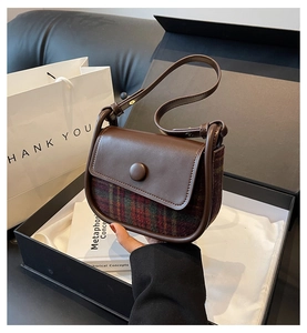 Detail of vintage saddle bag featuring red and green plaid fabric and brown leather flap