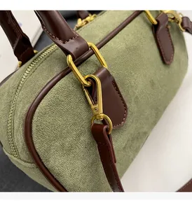 Dettaglio borsa in camoscio verde scuro con finiture dorate e bordi in pelle marrone